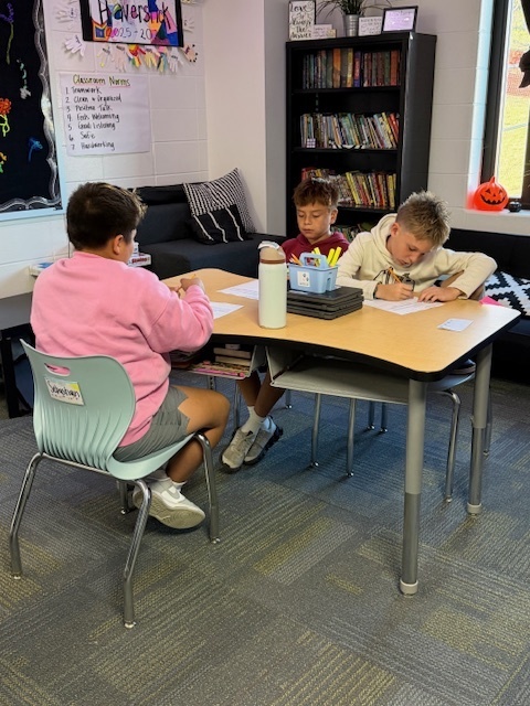 Students writing down what they are learning on papers at their desks.