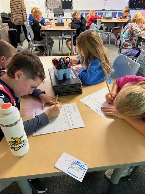 Students writing down what they are learning on papers at their desks.