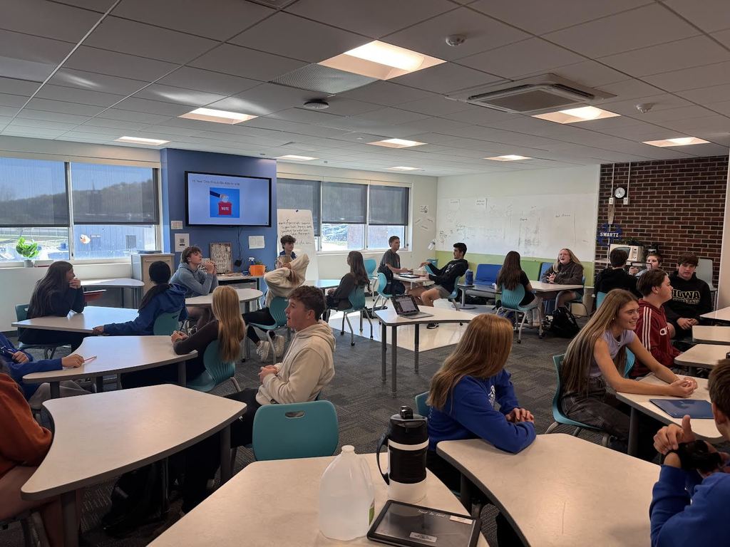 Students sitting at tables around the classroom debating each other.