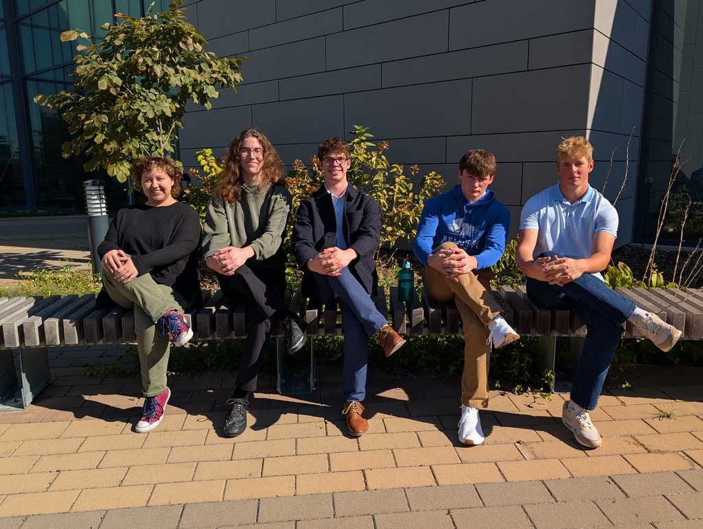 Five students sitting on a bench all in the same pose with their legs crosses and their hands on their knee.