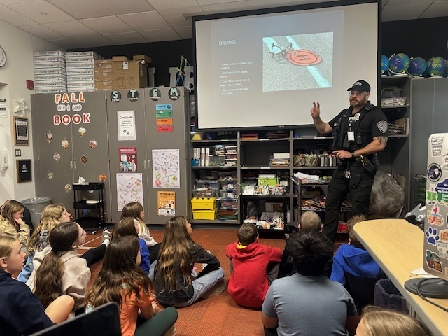 6th grade students sitting on the ground listening to the speaker, Officer Cooper.