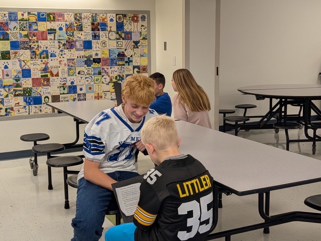 Two students sitting at a table, one reading the poetry to the other.