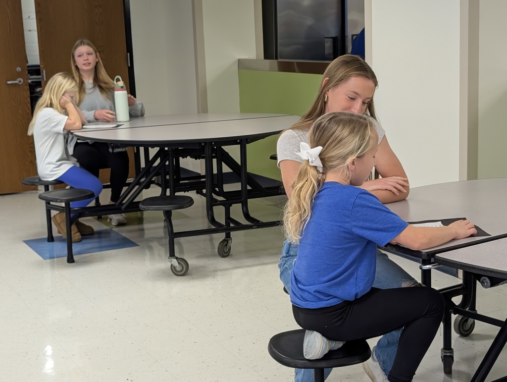 Students sitting at a tables listening and reading to each other.