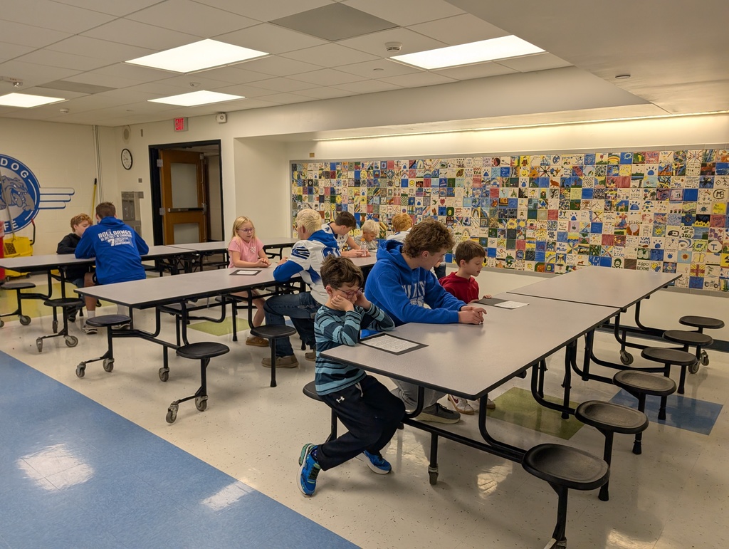 Students sitting at a tables listening and reading to each other.