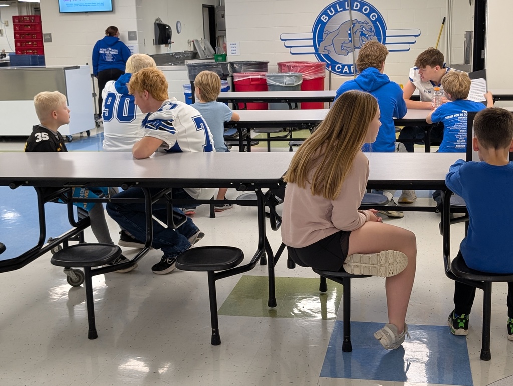 Students sitting at a tables listening and reading to each other.