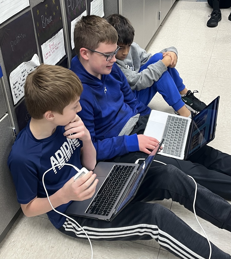 A 7th grader sitting on the floor and sharing his ebook with two 3rd graders.