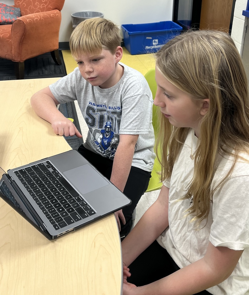 A 7th grader sitting at a desk and sharing her ebook with a 3rd grader.