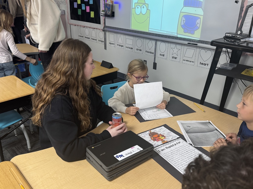 A high school student helping a second grader at a desk.