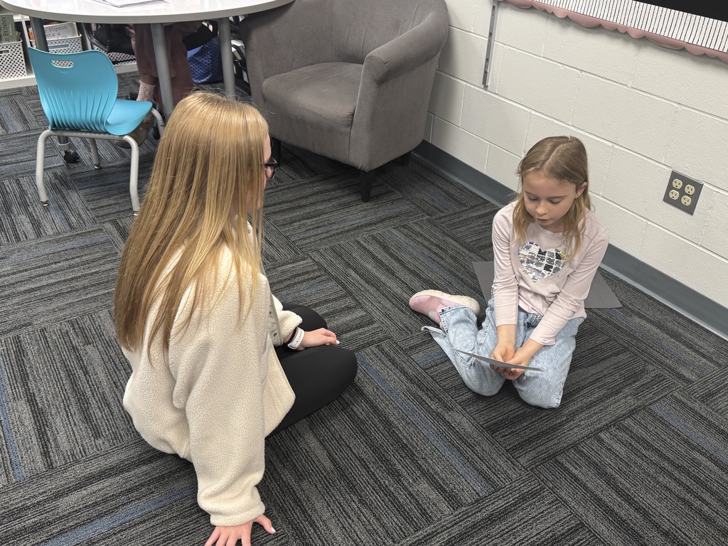 A high school student helping a second grader on a the floor.