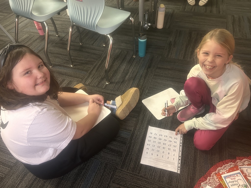 Two students sitting on the floor with their activity in their laps and smiling up at the camera