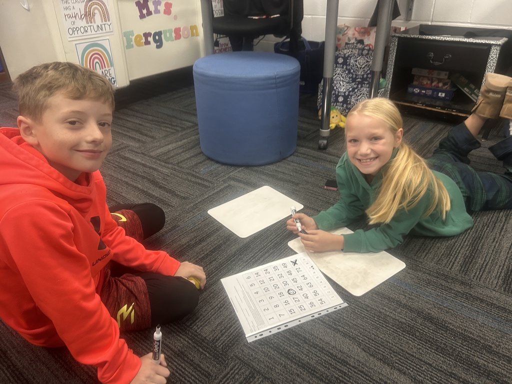 Two students on the ground with their whiteboards, markers, and activity sheet