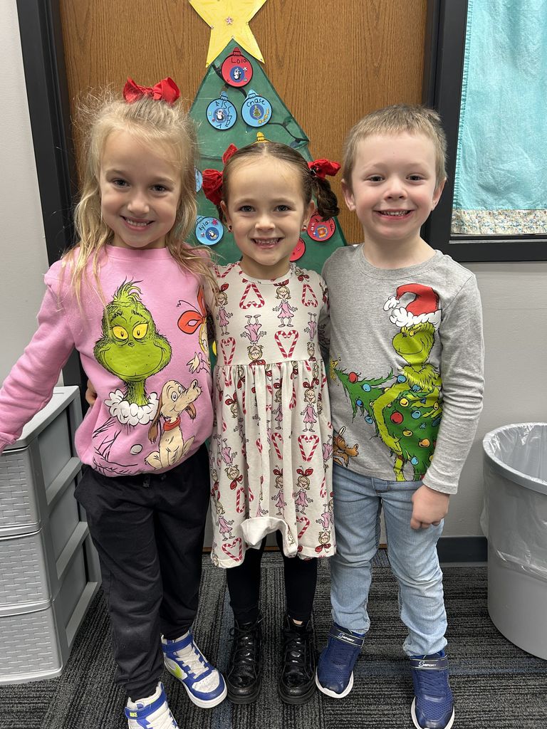 Three students with their festive clothing on standing in front of a door with a cut-out tree.