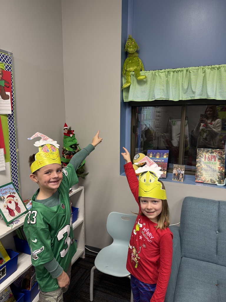 Two students with their grinch hats on pointing to where the grinch toy got himself stuck at.