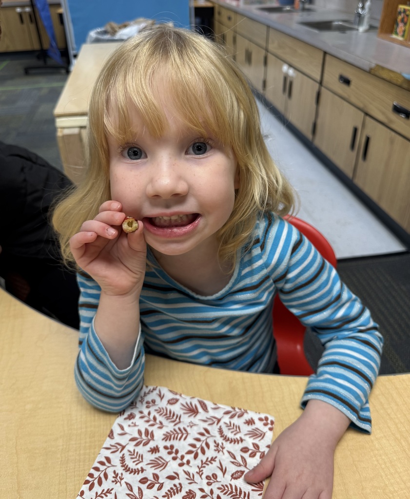 A student in a striped blue shirt holding a cranberry they had taken a bite of and smiling for the camera.