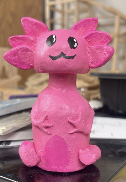 Bright pink axolotl figurine with large eyes and a smiling mouth, sitting upright on a black surface.