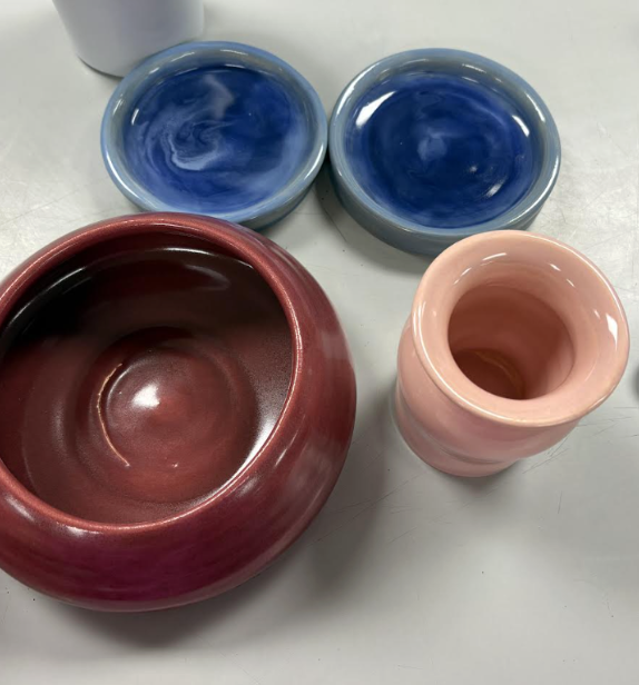Glossy ceramic bowls and a vase in red, blue, and pink hues arranged on a white surface.