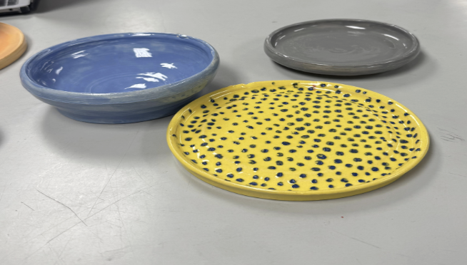 Yellow ceramic plate with blue polka dots next to a glossy blue bowl and a gray plate on a gray surface.
