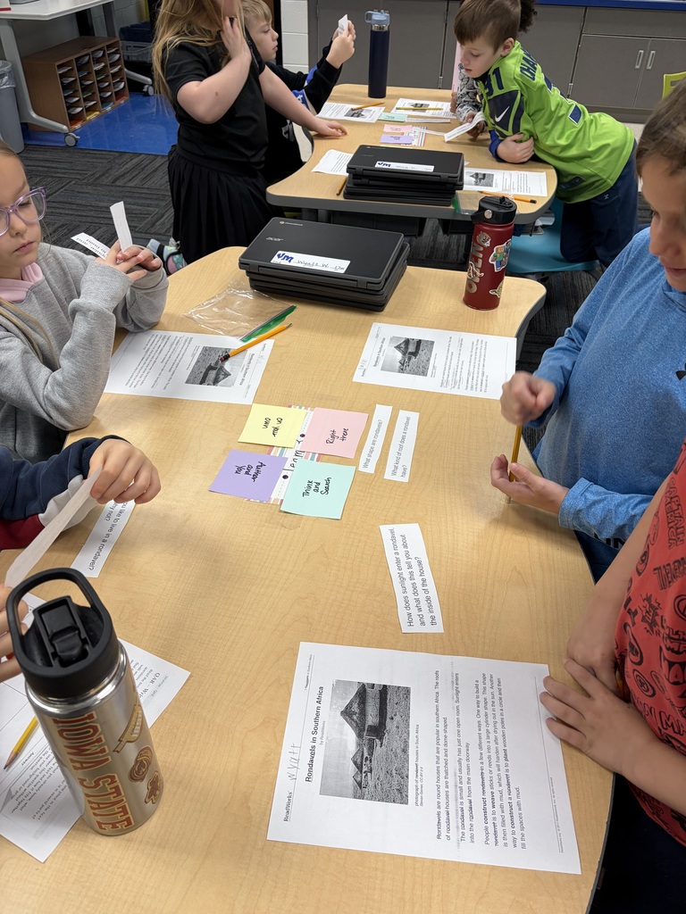2nd grade students engaged in a classroom activity sorting colorful paper cards and reading printed worksheets at a wooden table.