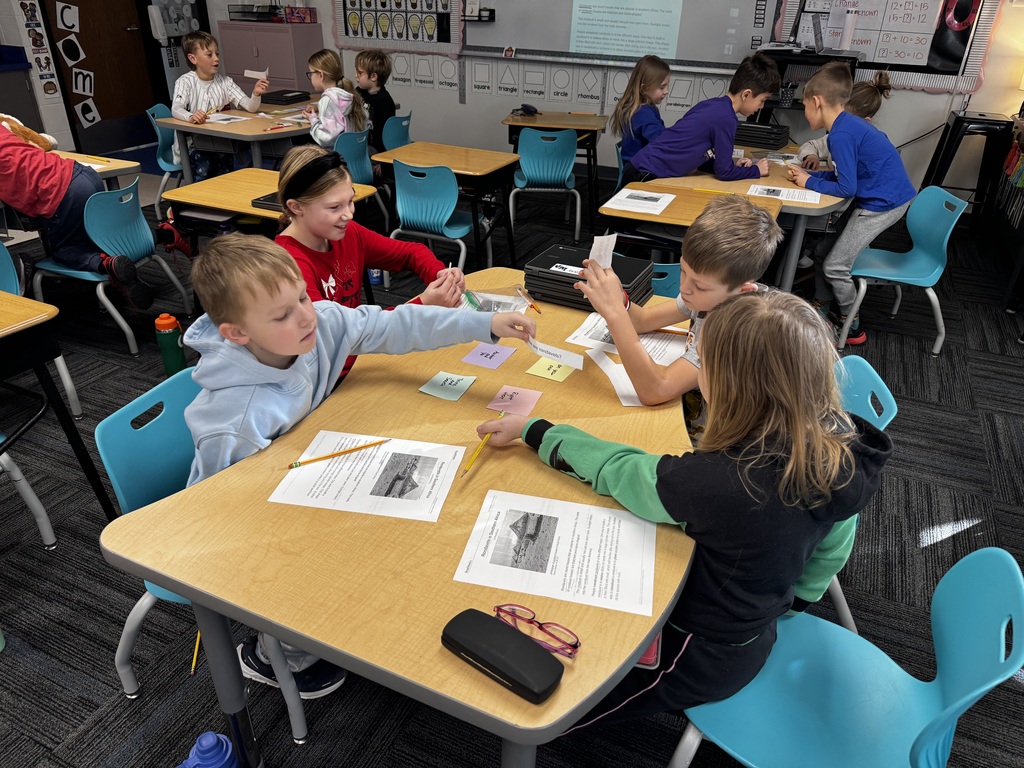 Van Meter 2nd grade students collaborate on a classroom activity using colored cards and worksheets at a shared table.