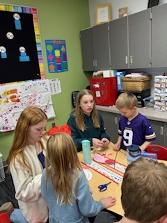 Van Meter students engaged in a classroom craft activity around a table with scissors and paper strips.
