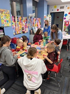 Van Meter students engaged in arts and crafts around a table in a colorful classroom decorated with artwork and educational posters.