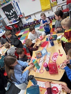 Van Meter students engaged in a colorful classroom activity, crafting and interacting around a table filled with supplies and toys.