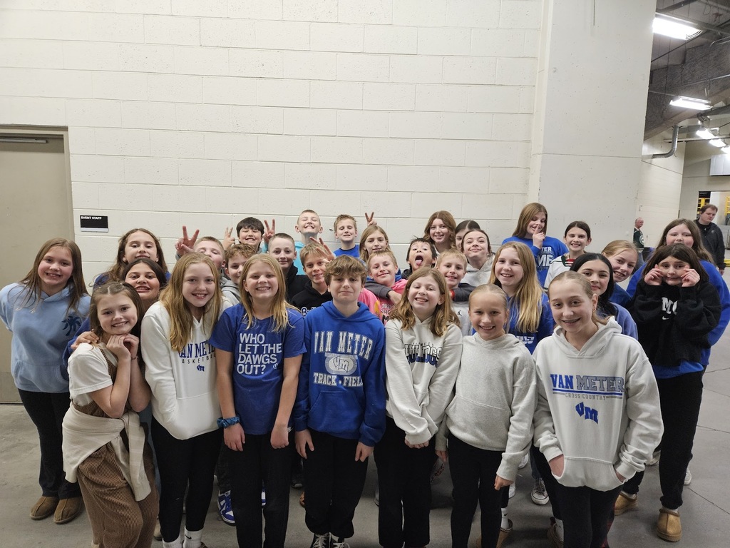 Group of young vocalists in Van Meter apparel posing together indoors against a white brick wall.