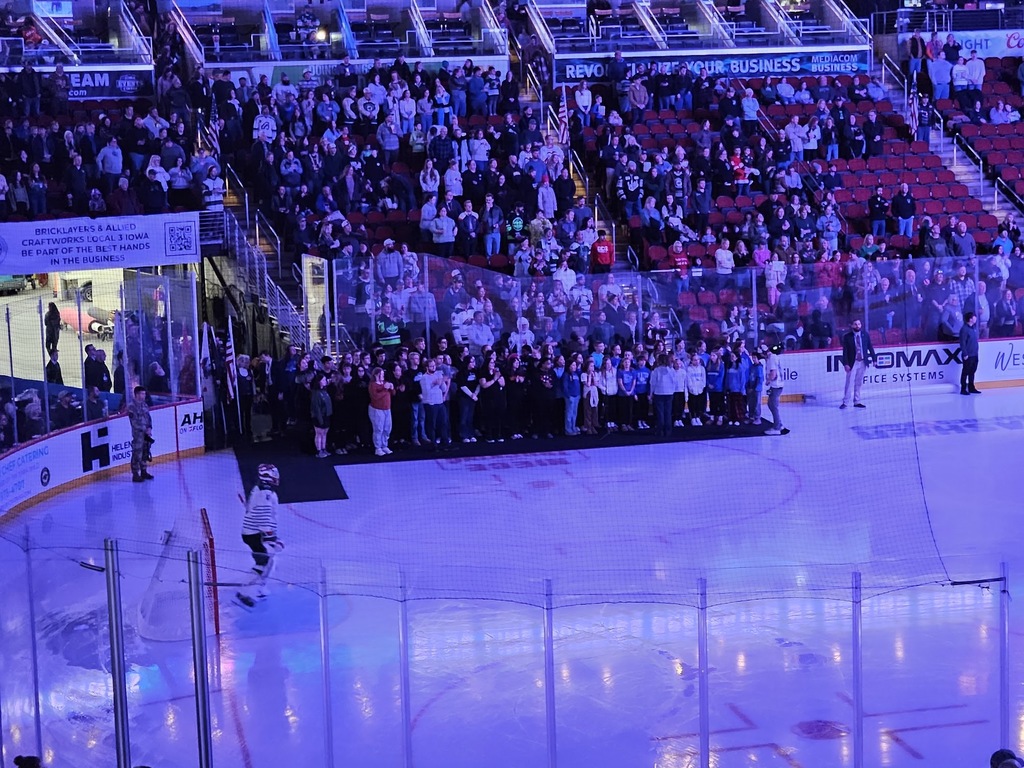 Large crowd gathered in arena stands watching the Van Meter students sign on the ice during the pre-game.