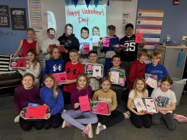 A class of students sitting, kneeling, and standing in rows holding donation gifts.