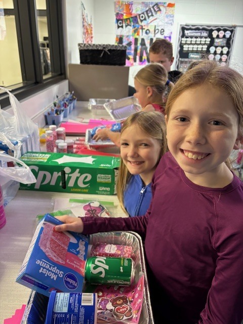 Children gathered around a table with snacks and drinks, including Sprite cans and packaged meat, in a colorful classroom setting.