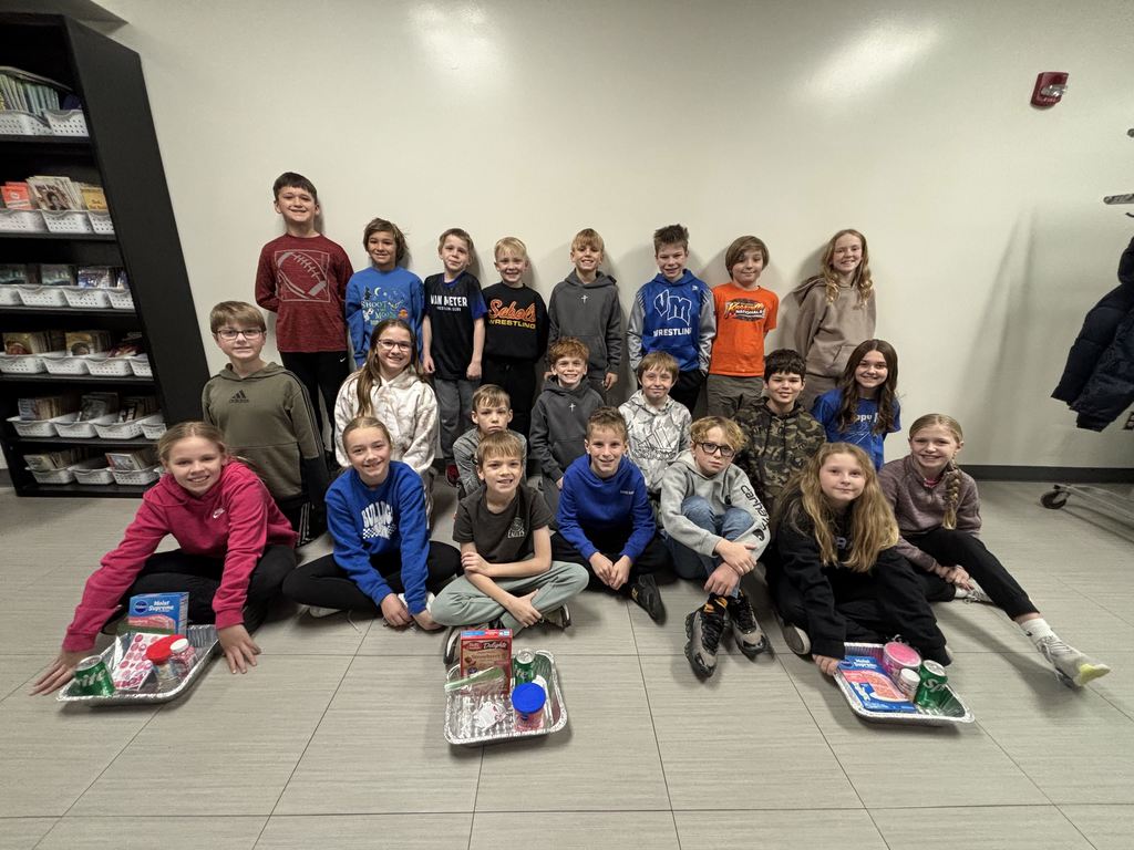 A class of students sitting, kneeling, and standing in rows with donation gifts in front of them.