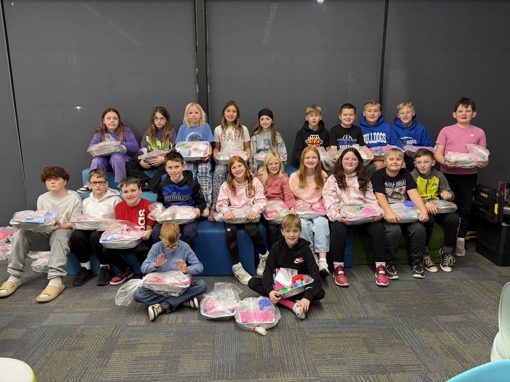 A class of students sitting in rows with donation gifts in front of them.