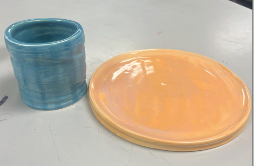 Glossy blue ceramic cup with a smooth finish next to a shiny orange ceramic plate on a light surface.