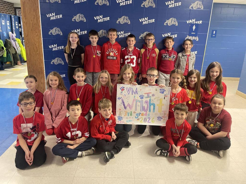 Group of elementary students wearing red shirts posing with a colorful 'VM Wright' sign in front of a Van Meter school backdrop.