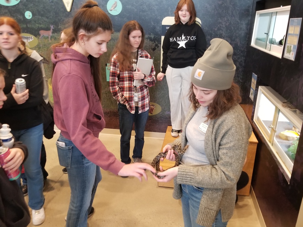 A group of young people gathered indoors, one woman holding a small snake while others observe closely.