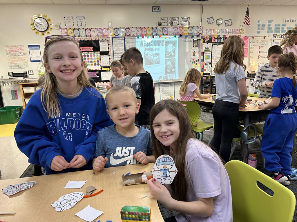 Elementary students engaged in a classroom craft activity, cutting and assembling paper snowman figures at a table.