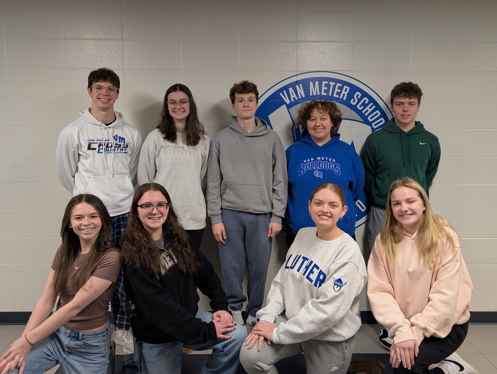 Group of nine students posing in front of a Van Meter School emblem on a beige wall indoors.