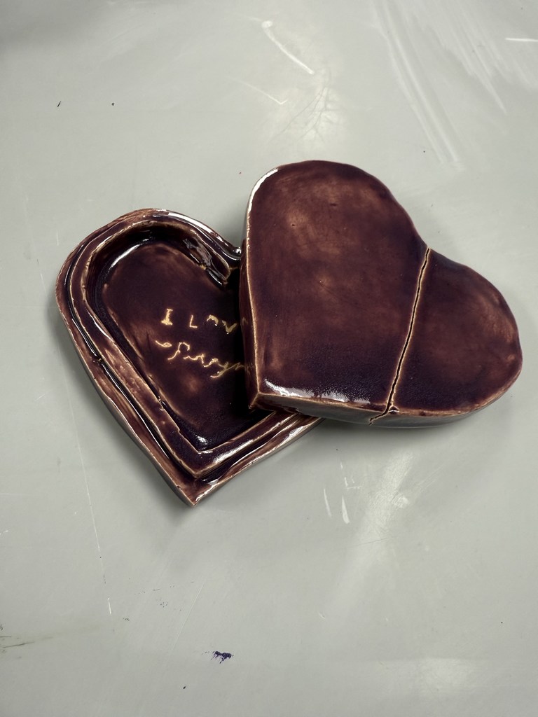 Glossy dark brown ceramic heart-shaped box with a removable lid resting beside the base on a light surface.