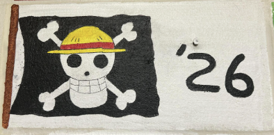 Black pirate flag with white skull and crossbones wearing a yellow straw hat, next to the number '26' on a white background.