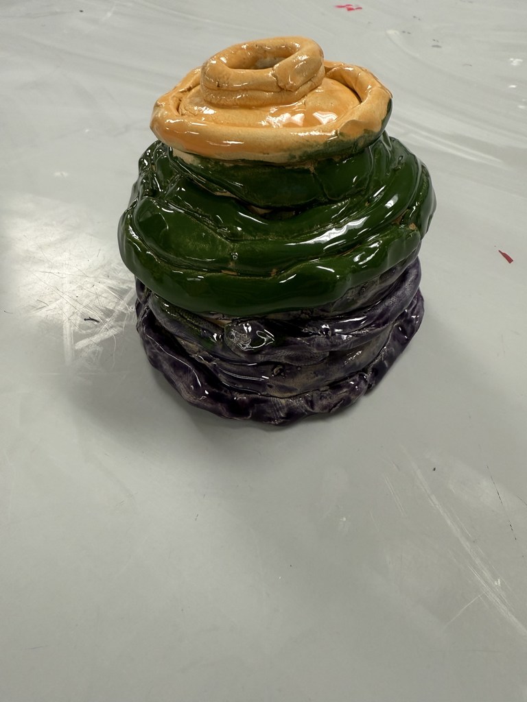 Glossy ceramic sculpture with stacked coils in orange, green, and purple hues on a white surface.