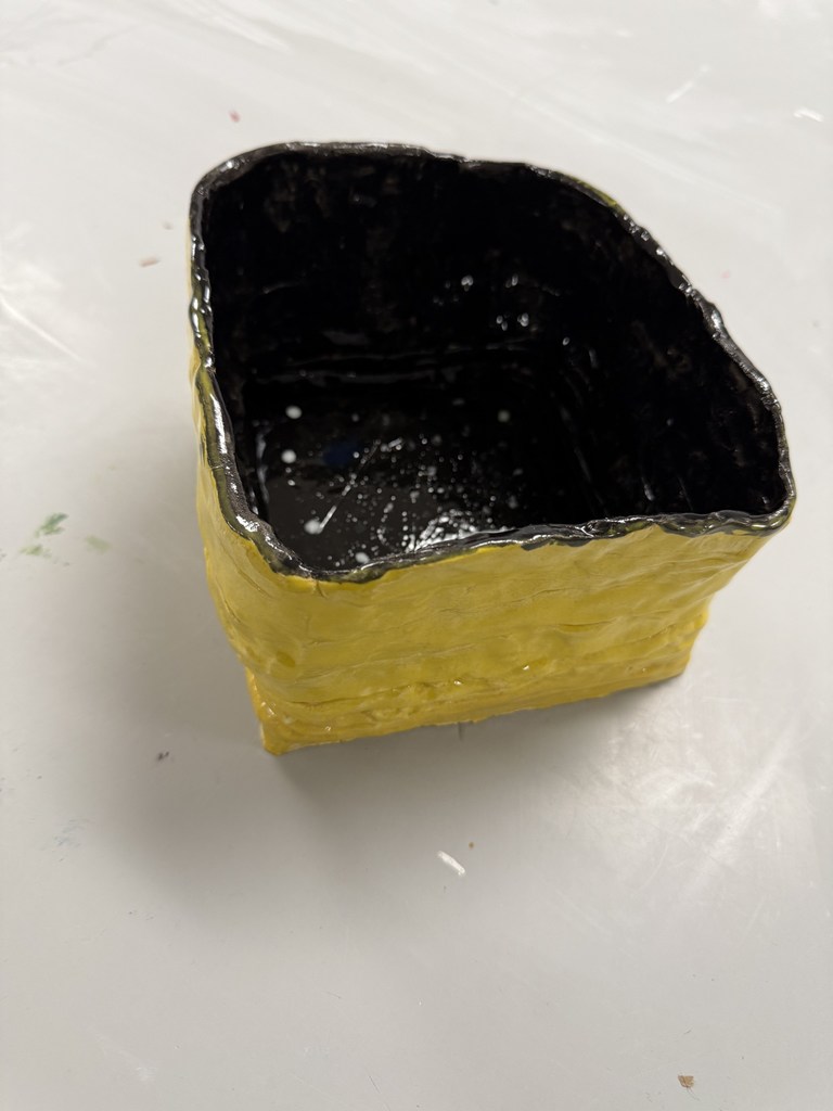 Small square ceramic pot with a glossy black interior and textured bright yellow exterior on a white surface.