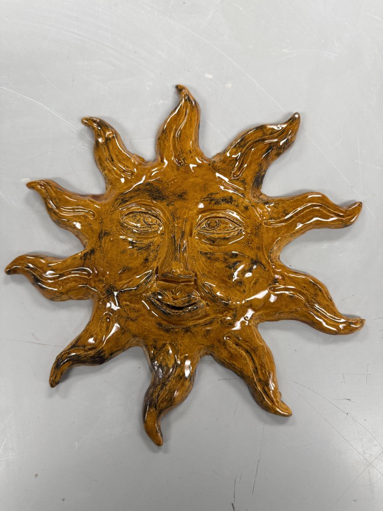Glossy ceramic sun sculpture with a smiling face and wavy rays on a light surface.