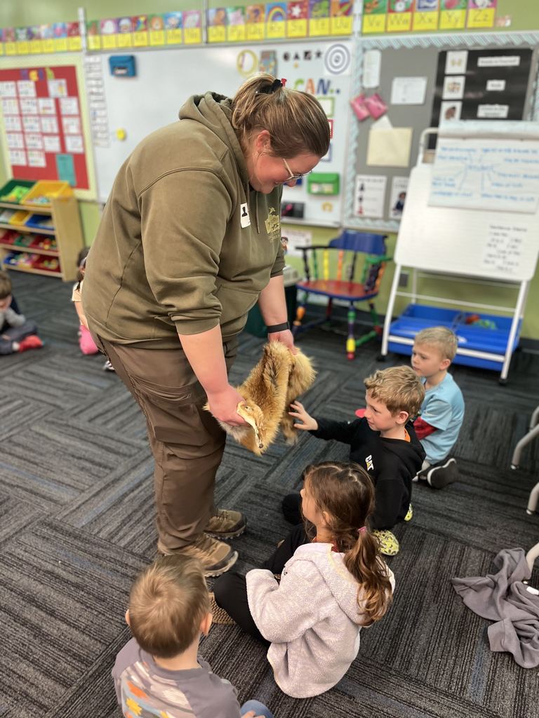 Teacher showing a furry animal pelt to a group of young children seated on a classroom carpet.