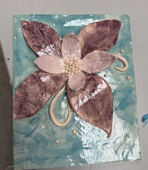 Glossy ceramic artwork of a large flower with five textured purple petals and a cluster of beige beads at the center on a turquoise background.