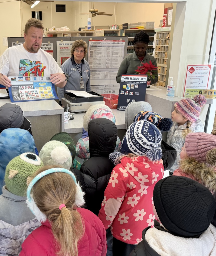 Postal worker shows a sheet of stamps to a group of bundled-up children gathered at the counter during a post office visit.