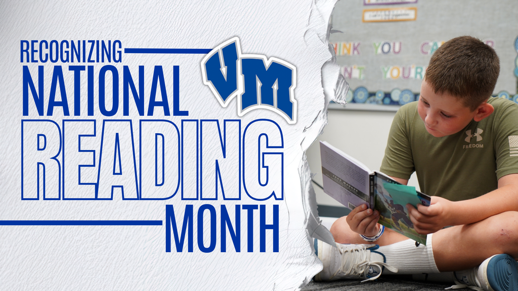 A young boy sitting cross-legged on the floor, focused on reading a book during National Reading Month at VM school.