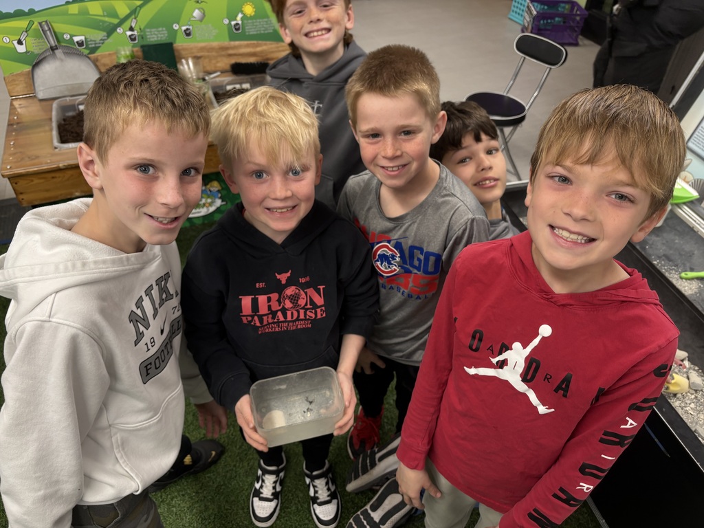 Group of smiling students pose together while holding a container with a sample from their hands-on science activity.