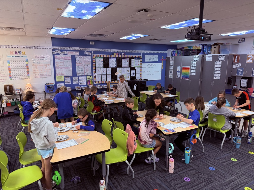 Students at multiple tables focus on hands-on sorting activity with worksheets and plates in a bright, organized classroom.