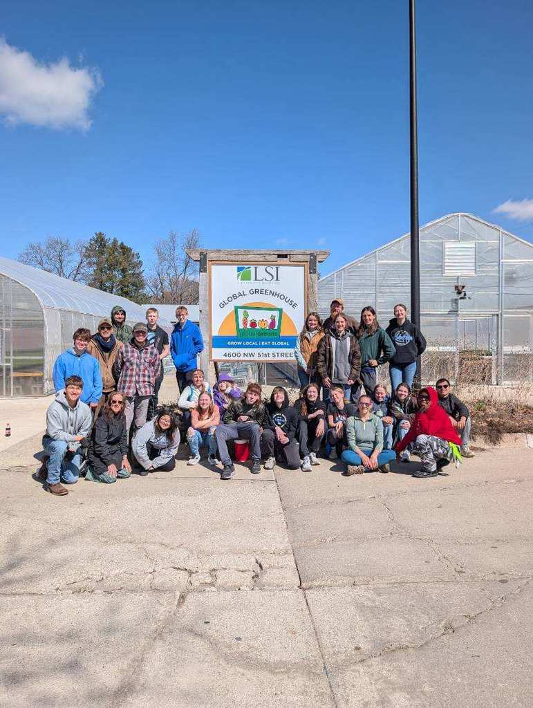 Group of people posing in front of LSI Global Greenhouse sign and greenhouses on a sunny day.