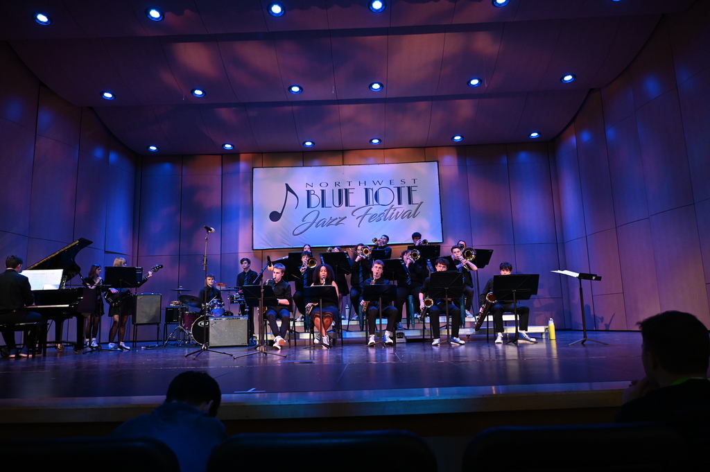 Jazz band performing on stage at the Northwest Blue Note Jazz Festival with various instruments under blue stage lights.